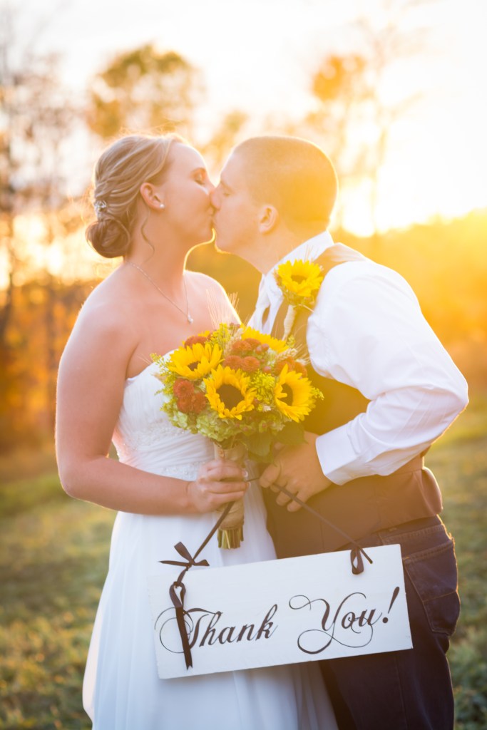 wedding couple kissing in the sunset holding a thank you sign